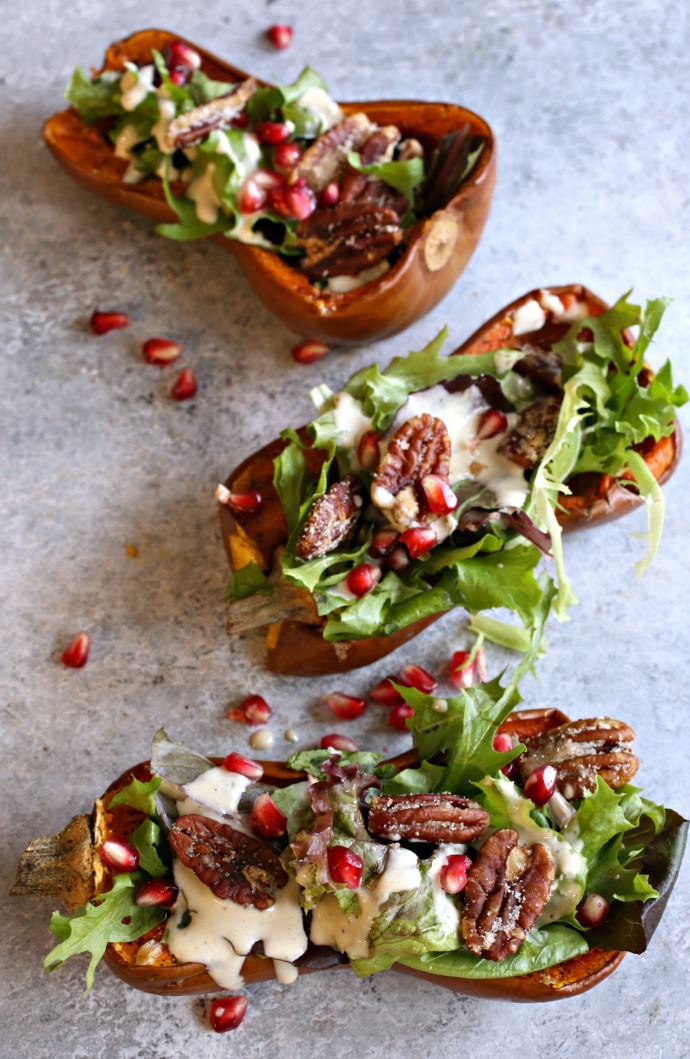 Recipe for salad served inside a roasted honeynut squash and topped with pomegranate arils, candied pecans and a tahini dressing.