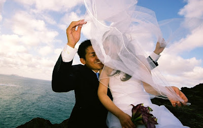 Groom holding her veil in the wind on the cliffs of Hawaii