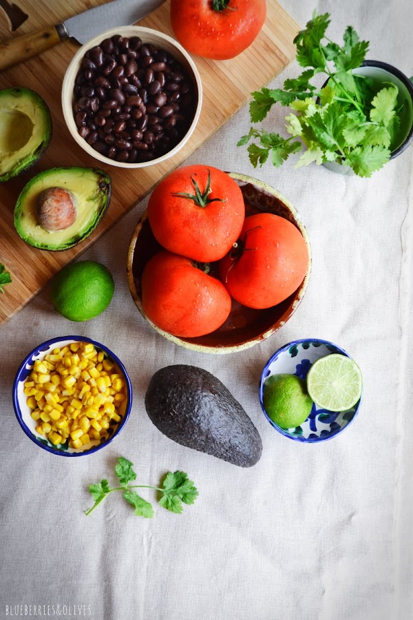 INGREDIENTES PARA TOMATES RELLENOS TEXMEX, FRIJOLES, AGUACATE, TOMATES, MAÍZ, CILANTRO, LIMA, SOBRE TABLA MADERA CORTAR, MANTEL LINO BEIGE