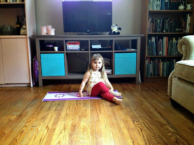Photo of young girl sitting on a yoga mat in the living room--with wooden floors