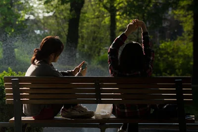two young girls resting in forest (one is texting on smartphone)