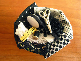 Dolls' house miniature sewing basket with various fabrics and notions in black and white, plus scissors and a tape measure.