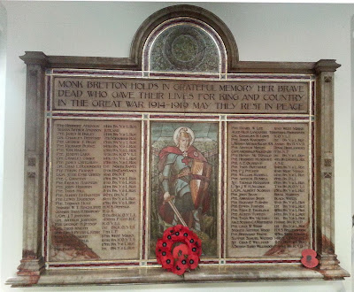 A large alabaster tablet.  The top section has the inscription "Monk Bretton holds in Grateful Memory her Brave Dead who gave their lives for King and Country in the Great War 1914-1919 May they Rest in Peace" surmounted by a semi circular extension enclosing a wreath.  Below are three panels, the central one holds a picture of St George, on either side are the lists of names.  The whole is surrounded by a mosaic border and carved raised borders in the stone.  There is a ledge below on which is resting a poppy wreath.