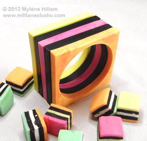 Yellow, black, pink, black and orange square bangle stack look like layers of a licorice allsort.