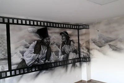 Artystyczne malowanie ściany w pokoju telewizyjnym, aranżacja sciany w sali telewizyjnejj poprzez malowanie, czarno-biały obraz namalowany na ścianie, motyw z filmu Janosik