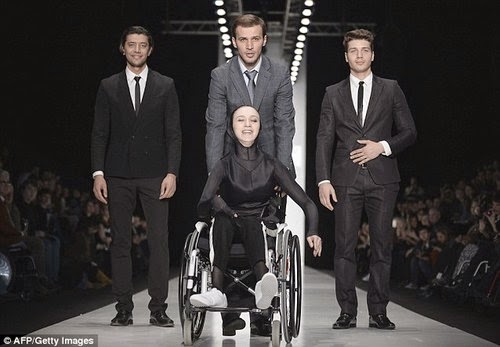 three men and one woman in a fashion show pose, woman is in wheelchair, men standing behind her