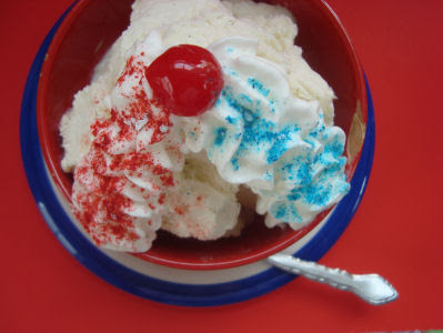 Sundae with cherry on top and two whipped cream lines one with red and one with blue sprinkles