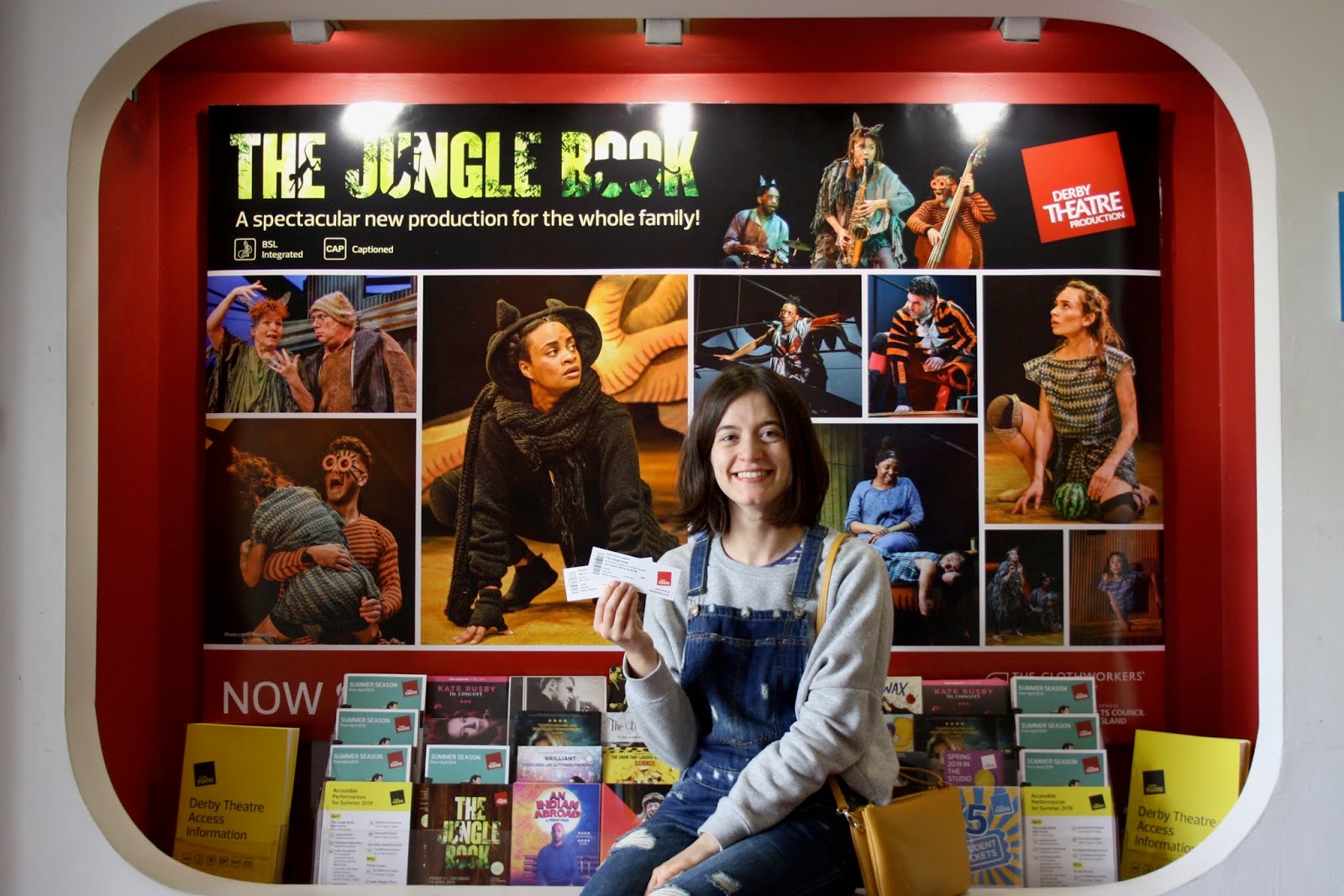 Abbey holding her tickets to The Jungle Book, seated before a poster advertising the performance at Derby Theatre