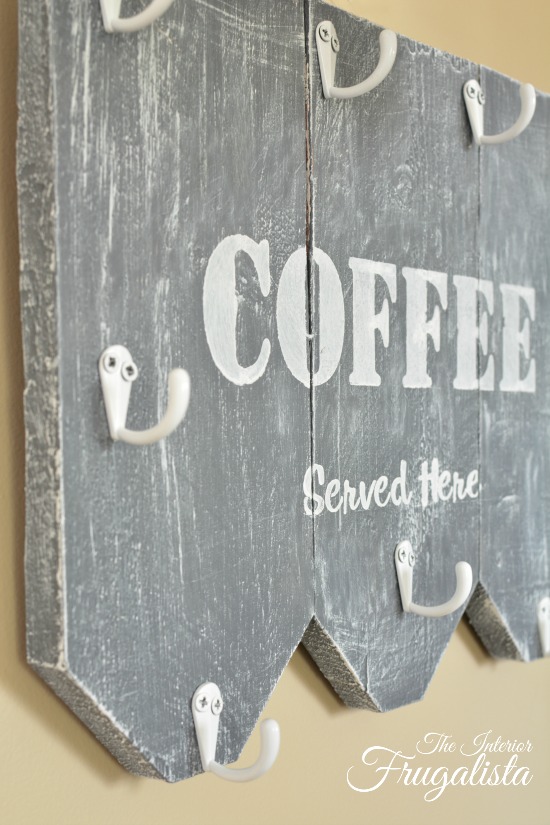 Stenciled wooden coffee mug holder with white hooks.