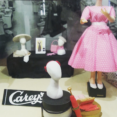 Model of a draper's front window with mannequins displaying frocks and hats.
