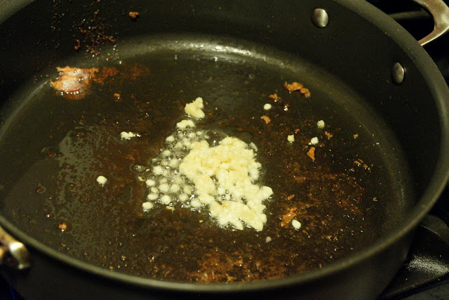 The minced garlic being added to the bacon fat in the hot skillet. 