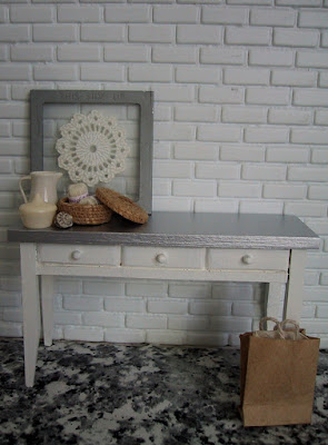 Modern dolls' house miniature white side table with a zinc top. On it are displayed a number of accessories in grey, white and natural.