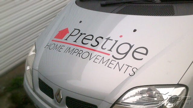 Prestige Home Improvements logo on the bonnet of the renault car. The logo is in black and red featuring a red house. The 'i' in prestige has a red dot.