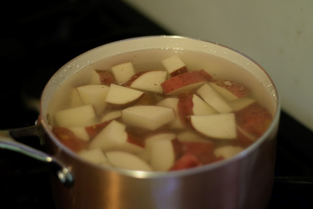 The diced red potatoes in a pot with water, on the stove. 