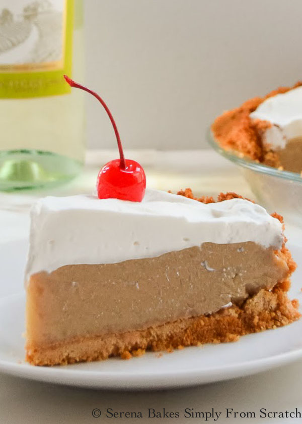 A slice of Frozen Root Beer Float Pie covered with sweetened whipping cream and topped with a cherry on a white plate.