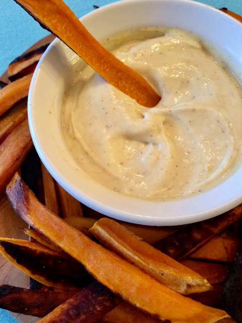 Baked sweet potato fry being dipped into creamy maple mustard dipping sauce.