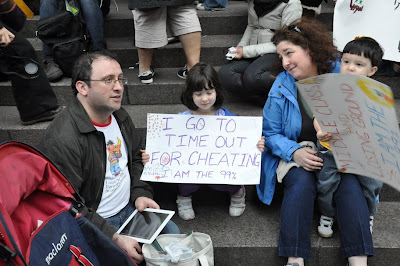 Photograph of family at Zuccotti Park. The little girl’s sign reads “I go to time out for cheating. I am the 99%.”