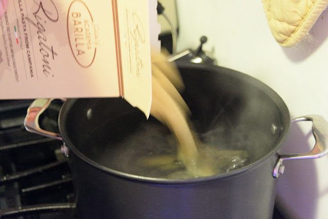 Pasta being poured into the boil pot of water on the stove. 