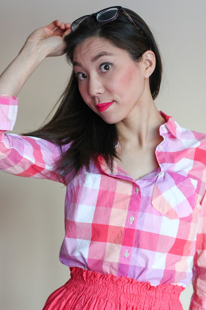 [Image of a tan skin bespectacled Asian woman wearing a plaid pink button down tucked into an elastic waist A-line coral skirt she made for herself years ago. Her dark brown hair is down. She's holding her glasses up on top of her head and smiling at the camera without actually being able to see where the camera is.]