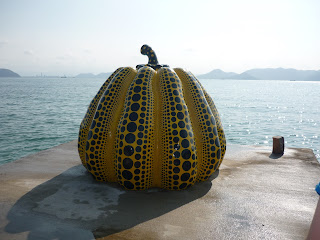 Famous Naoshima pumkin. It is about as tall as a person, yellow with black spots and is located in a platform that juts out a little into the ocean