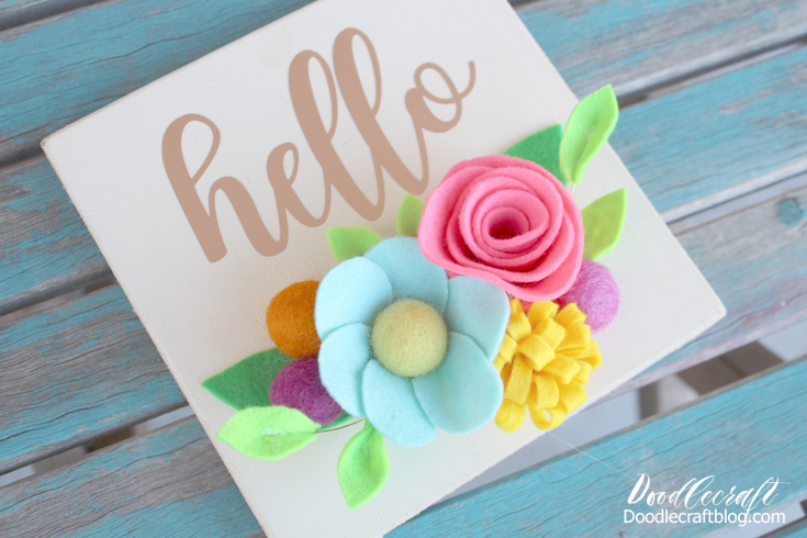 Hello Vinyl Wood Sign with Bright Felt Flowers! Isn't this hello sign perfectly bright and cheery with these colorful felt flowers!? Just a few supplies make this perfect Spring decoration for the mantle, bookshelf or in the entryway. Let me show you how to make felt flowers to add color to a vinyl wood sign for the perfect home decor piece!  It's super simple to make and then options are endless when it comes to adding a greeting.  Let's craft this cute sign in less than an hour!  Make a bunch and sell them at a Spring craft show--they will fly off the shelf!