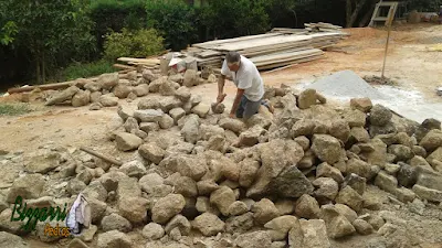 Bizzarri trabalhando, fazendo o corte das pedras moledo para fazer o revestimento de pedra na parede, com pedra moledo na cor bege com espessura de 15 a 20 cm.