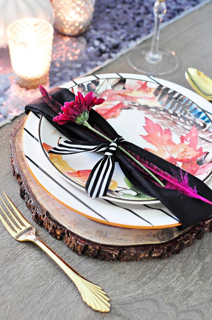 A rustic glam fall floral tablescape featuring a bold floral pumpkin centerpiece, acacia wood chargers, black and white striped dinner plates and leaf salad plates paired with vintage gold flatware. A colorful, metallic glam look perfect for any fall dining table. 