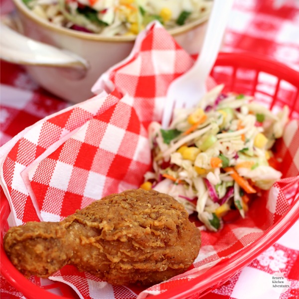 Fried chicken leg and Firecracker Coleslaw by Renee's Kitchen Adventures with a fork ready to eat in a white and red checkered lined basket