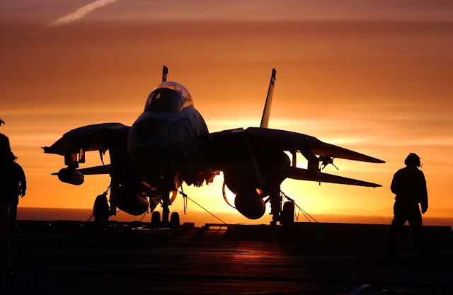 F-14D tied down on the deck with the sun setting.