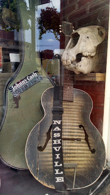 Old guitar, guitar case with Johnny Cash sticker, and skull in window display