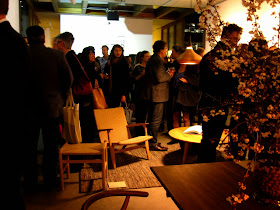 Crowd at a gallery opening. A Hans Wegner table and chair are in the foreground and a stool, armchair and coffee table in the background.