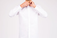 A Man buttoning the top button on a very white shirt in a very white background