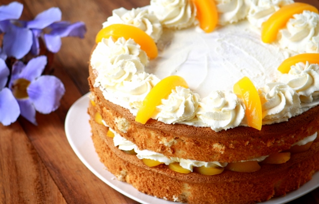 Torta de crema y duraznos sobre un plato blanco. flores lilas al costado izquierdo