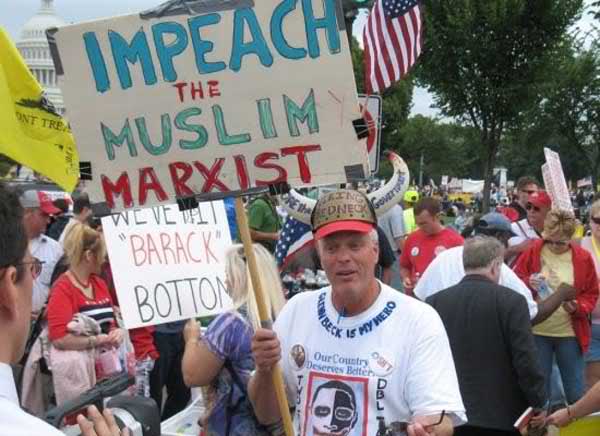 Unnamed protester at the Taxpayer March on Washington (September 12, 2009). It shows a man, standing among a crowd of protesters near the capitol building in Washington D.C., holding a sign that says "IMPEACH THE MUSLIM MARXIST" and around the collar of his T-shirt is written "GLENN BECK IS MY HERO."