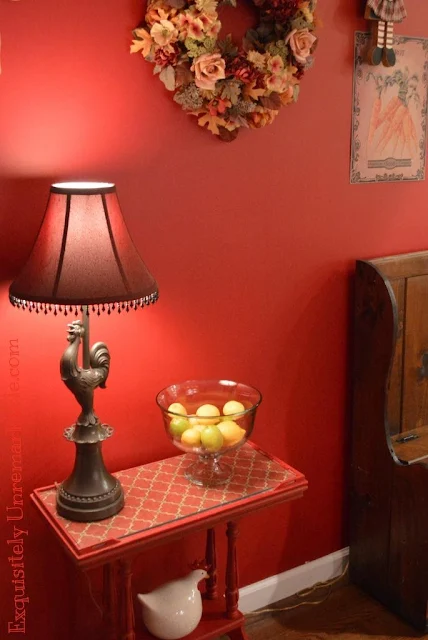 A little red table with fabric under glass and a rooster lamp in the kitchen