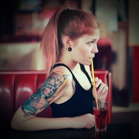 chica sentda en un bar bebiendo soda, lleva tatuaje de india y lobo