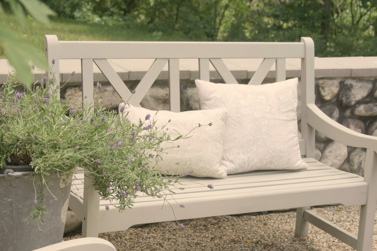 Light grey bench in pea gravel French inspired courtyard with lavender in bucket - Hello Lovely Studio