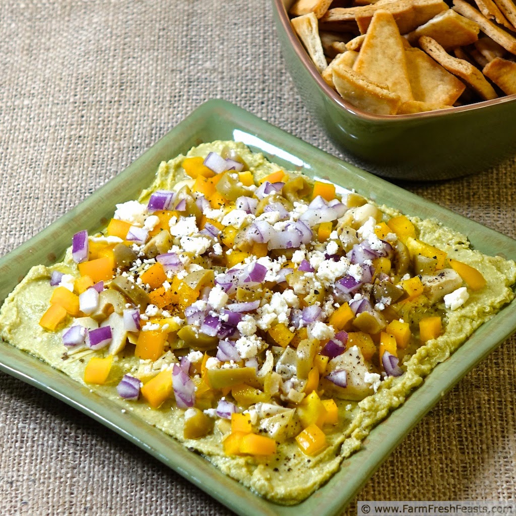 photo of Avocado feta hummus served as a layered appetizer topped with feta cheese, red onion, green olives, and yellow peppers