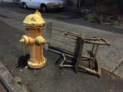 a wooden rocking chair passes out by a fire hydrant.