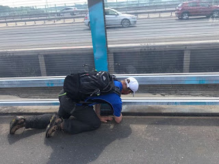 Ein Mann kniet auf dem Boden. Im Hintergrund die Autobahn