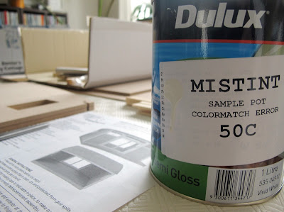 One litre tin of mistint paint, marked 50c, on a table in front of pieces of a dolls' house miniature kit.