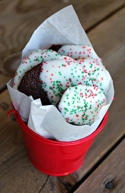 chocolate cookies dipped in white chocolate and covered in holiday sprinkles shown in a red pail