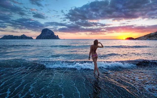 Vrouw in bikini loopt de zee in tijdens een zonsondergang op het strand van Ibiza.
