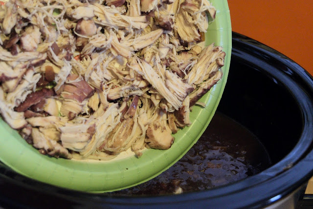The shredded chicken being added to the crock pot.