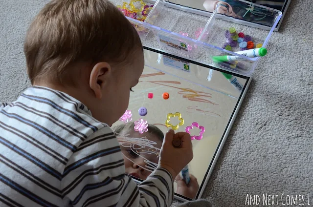 Young child drawing on mirrors with window markers as part of a spring themed invitation to play