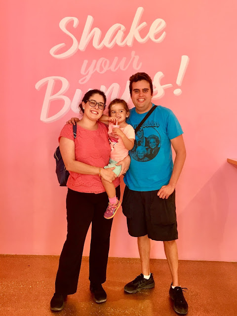 A family of three in front of a pink wall with white letters reading, "Shake your Bunns!"