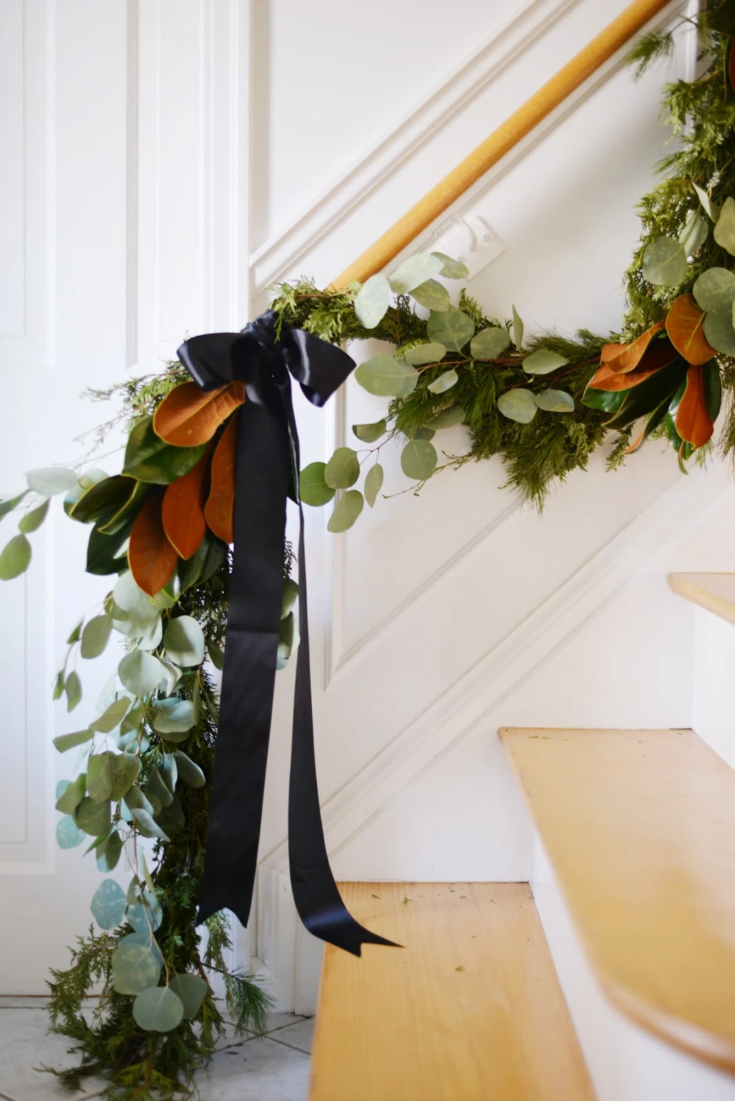christmas garland swag on staircase with pine cedar magnolia silver dollar eucalyptus and black satin ribbon