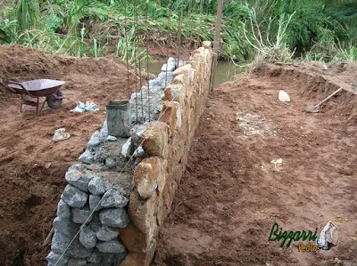 Construção do muro de pedra com pedra bruta para a base da construção da ponte de concreto na entrada da empresa em Atibaia-SP.