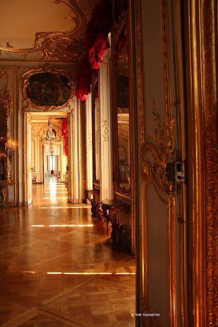 Three open doors leading into high ceilinged gold-ornamented rooms