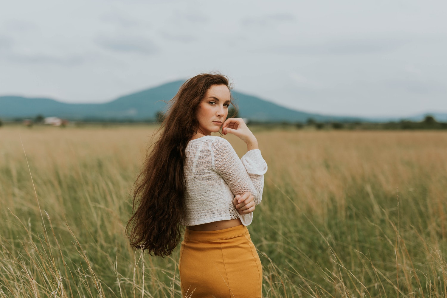 beautiful ginger woman with long, curly hair is posing in the field